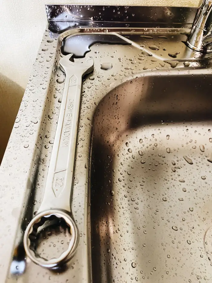 Close-up of a metal wrench resting on a stainless steel sink with water droplets